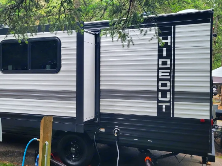 This Hideout RV rental is set up at a wooded campsite, featuring a slide-out and full utility hookups for a comfortable stay.. Keystone RV Hideout Sport 2024