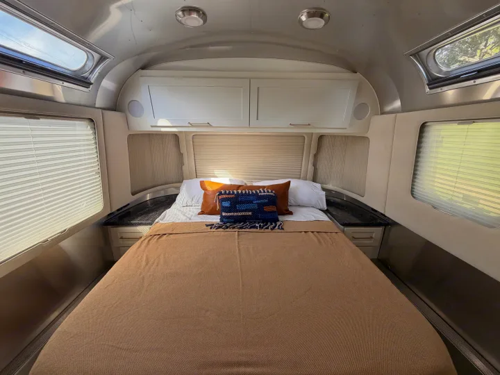 A well-appointed Airstream RV rental bedroom: bed, overhead cabinets, windows, and skylights for a bright, airy feel.. Airstream Classic 2021