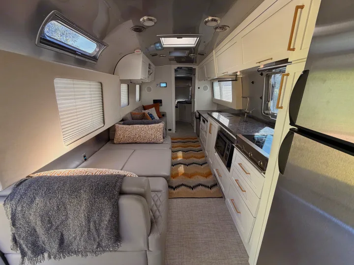 Explore this stylish rv rental with a sleek kitchen, cozy grey seating, and a chic rug. Ready for adventure!. Airstream Classic 2021