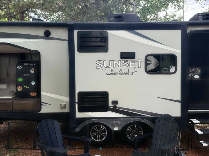 RV rental: Sunset Trail Grand Reserve travel trailer with outdoor kitchen & Adirondack chairs at a scenic campsite.. Crossroads RV Sunset Trail Grand Reserve 2017