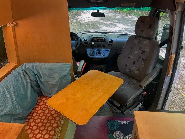 Inside an RV rental: custom camper van interior featuring wooden table, comfy seating, and driver's area view.. Dodge Sprinter 2005