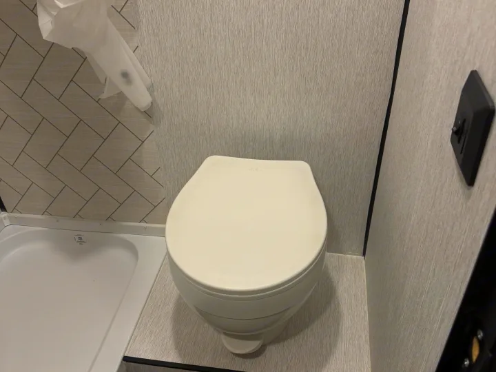 Clean RV rental bathroom featuring a white toilet, shower pan, and modern gray textured walls.. Sunset Park RV Sun Lite LTD 2024