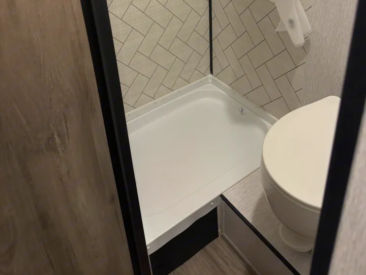 Compact RV rental bathroom featuring a white shower base, gray patterned walls, and a toilet. Essential comfort for your journey.. Sunset Park RV Sun Lite LTD 2024