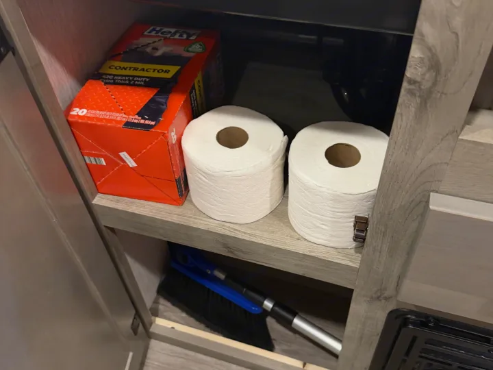 Essentials for an RV rental: Hefty contractor bags, toilet paper, and a broom organized in a compact cabinet.. Sunset Park RV Sun Lite LTD 2024