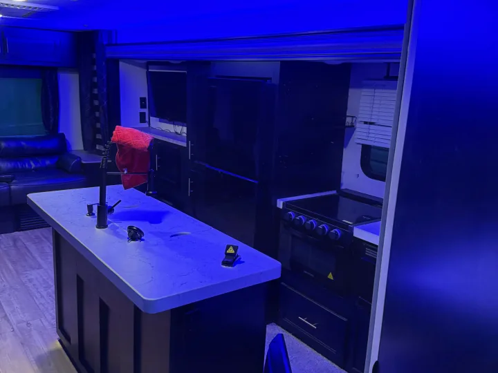 Interior of an RV rental: blue-hued kitchen island, stove, fridge, and lounge with dark furniture.. Forest River Cherokee 2023