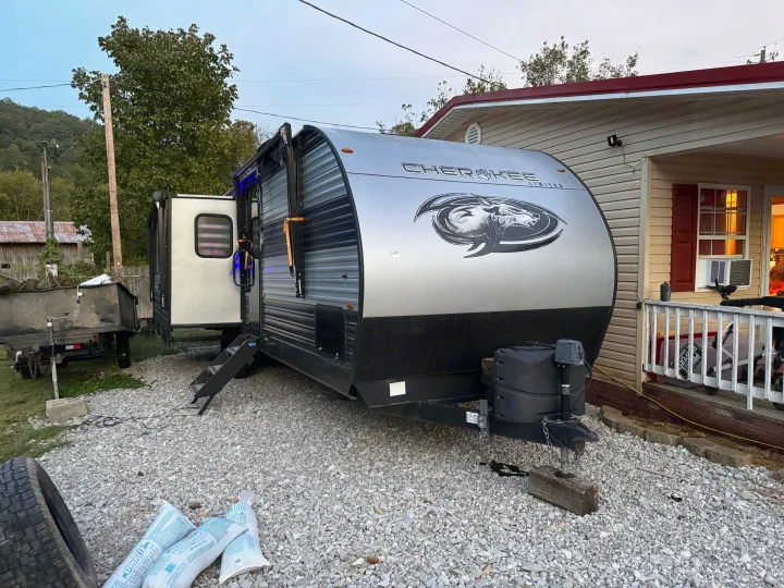 Cherokee Limited RV rental parked on gravel by a house. Its door is open, showing blue lights, providing a cozy outdoor scene.. Forest River Cherokee 2023