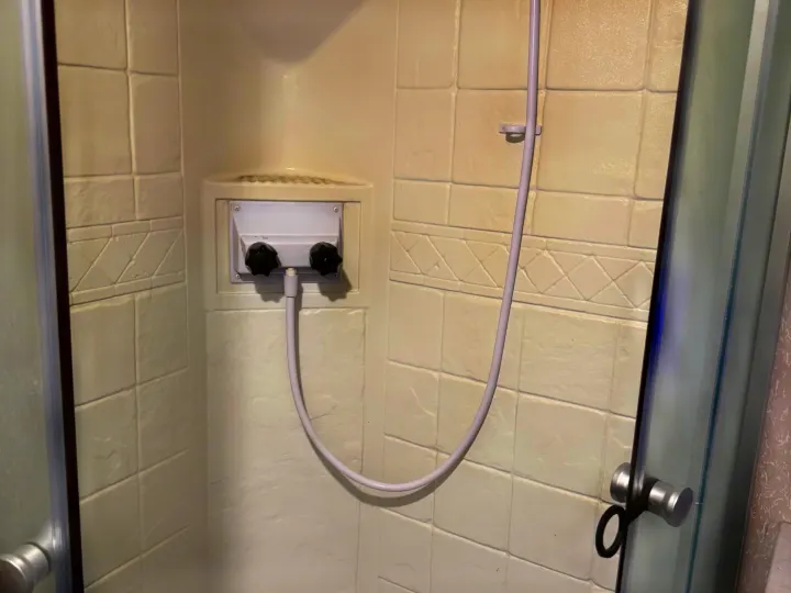 RV rental shower stall with dual-knob controls, flexible shower head, and cream tile-patterned walls. Note corner discoloration.. Forest River Cherokee 2023