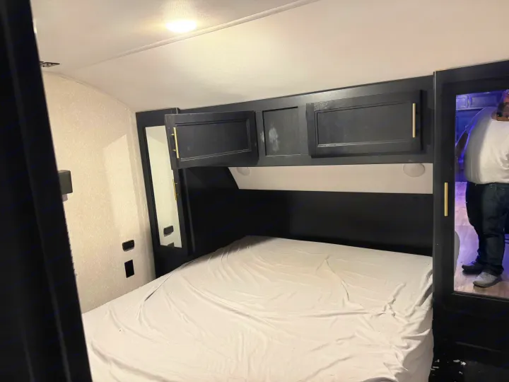 RV rental bedroom: a compact space with a white bed, dark overhead cabinets, and mirrored sides. Functional design.. Forest River Cherokee 2023