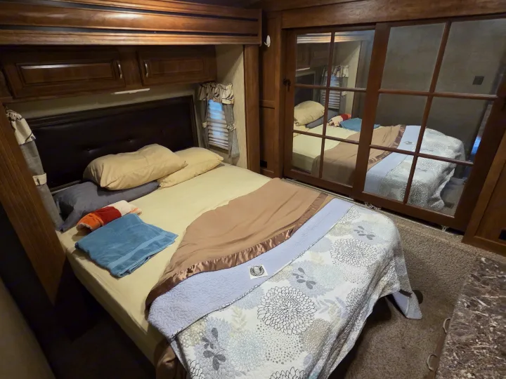Cozy RV rental bedroom featuring a comfortable bed, overhead cabinets, a small window, and a mirrored closet.. Keystone RV Laredo 2016