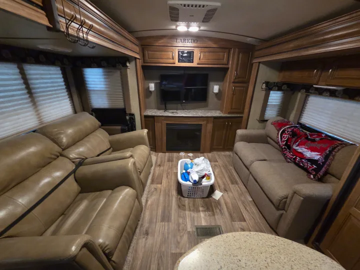 Comfortable Laredo RV rental interior shows living area with leather recliners, fabric sofa, TV, fireplace, and wood cabinetry.. Keystone RV Laredo 2016