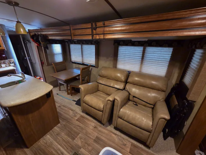Cozy RV rental interior features a kitchen counter, dining area, and two comfy recliners, ideal for travel comfort.. Keystone RV Laredo 2016