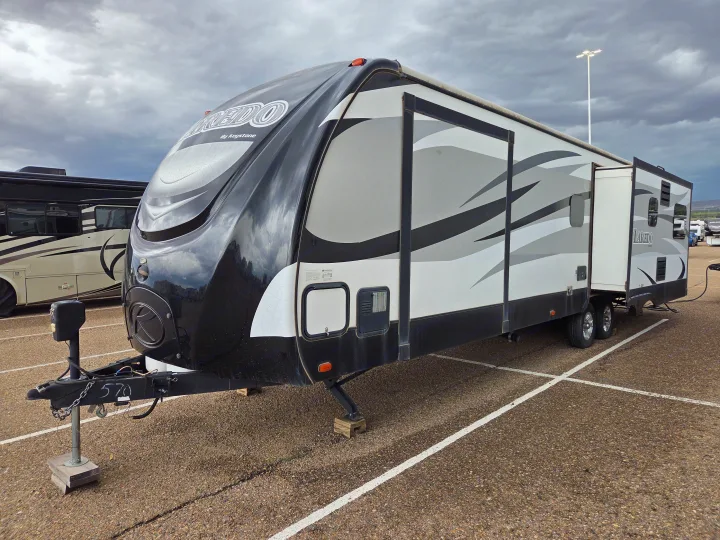 A large black, white, & gray Keystone Laredo rv rental, a travel trailer with an extended slide-out, parked on asphalt.. Keystone RV Laredo 2016