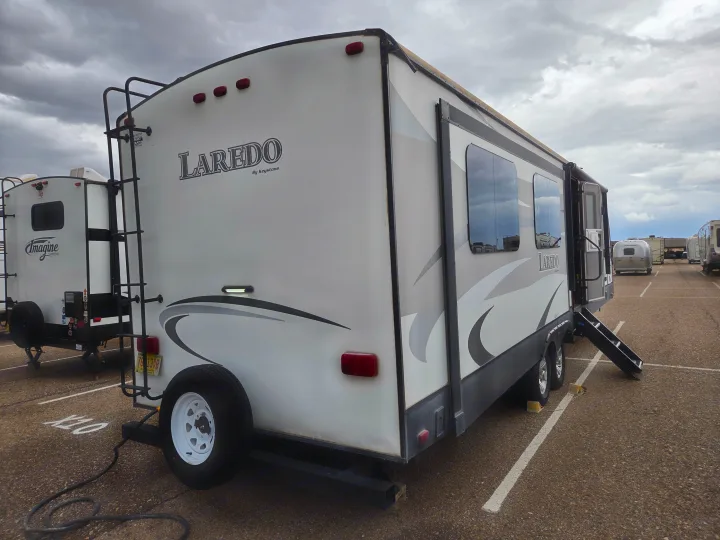 White Laredo travel trailer RV rental, with ladder, spare tire, and open steps, parked under cloudy sky.. Keystone RV Laredo 2016