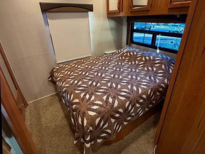 Cozy RV rental bedroom interior with a patterned quilt on the bed, window view, and wooden cabinetry.. Jayco Greyhawk 2016