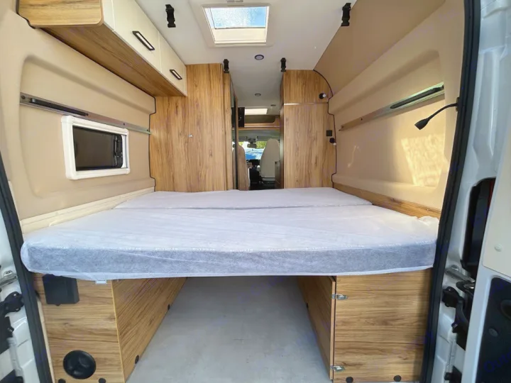 Explore this bright rv rental campervan interior, featuring a large, clean rear bed, sleek wooden storage, and a ceiling skylight.. Font Vendôme Leader Camper Duo 2024