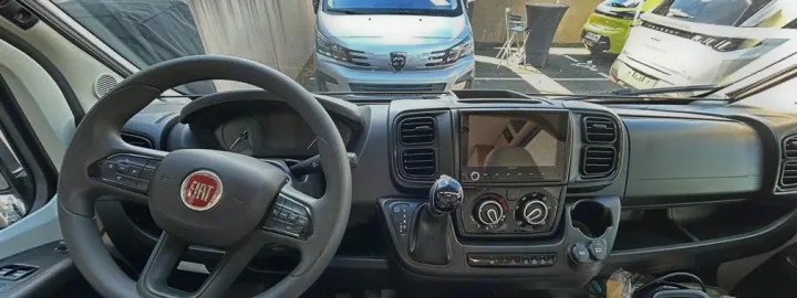 RV rental interior: Fiat dashboard with steering wheel, infotainment screen, and climate controls, seen from the driver's seat.. Font Vendôme Leader Camper Duo 2024