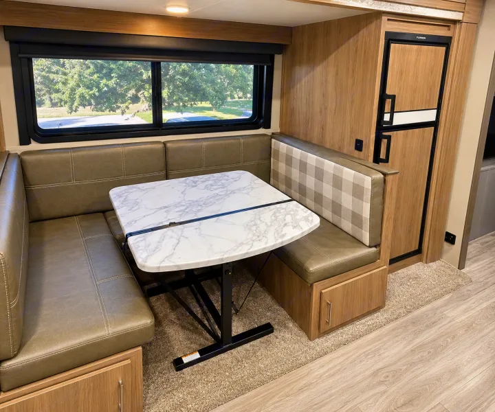 RV rental dinette features U-shaped seating, a marble-look table, large window with outdoor view, and a built-in fridge.. Grand Design Imagine 2021