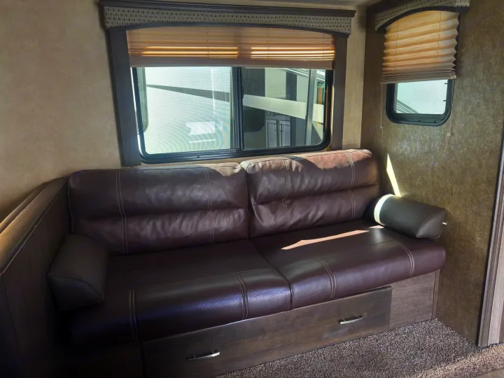 Comfortable brown leather couch with storage drawers and windows inside an RV rental for your next adventure.. Forest River 270BHS 2016