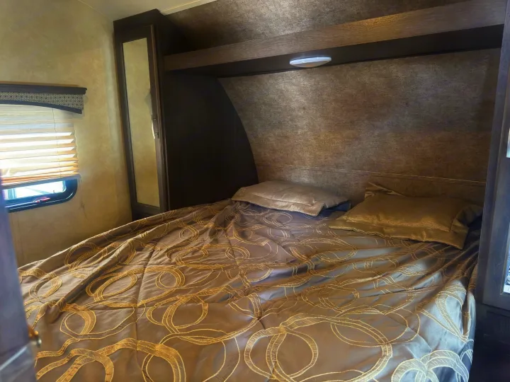 Step into a comfortable RV rental bedroom, featuring a patterned comforter on the bed, overhead shelf, and window blinds.. Forest River 270BHS 2016