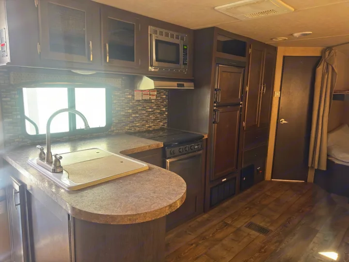 Experience comfortable travel in this RV rental's well-appointed kitchen, featuring a sink, stove, microwave, and ample cabinets.. Forest River 270BHS 2016