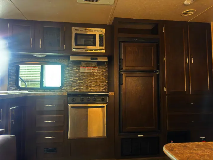 RV rental kitchen: Dark wood cabinets, microwave, stove, & refrigerator offer cooking essentials in this camper.. Forest River 270BHS 2016