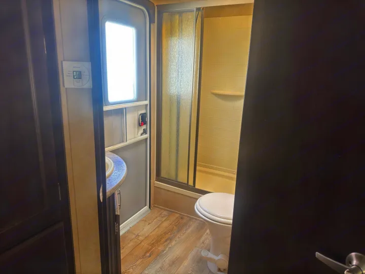 This RV rental bathroom features a compact shower, toilet, and a vanity with a sink, all with wood-look flooring.. Forest River 270BHS 2016
