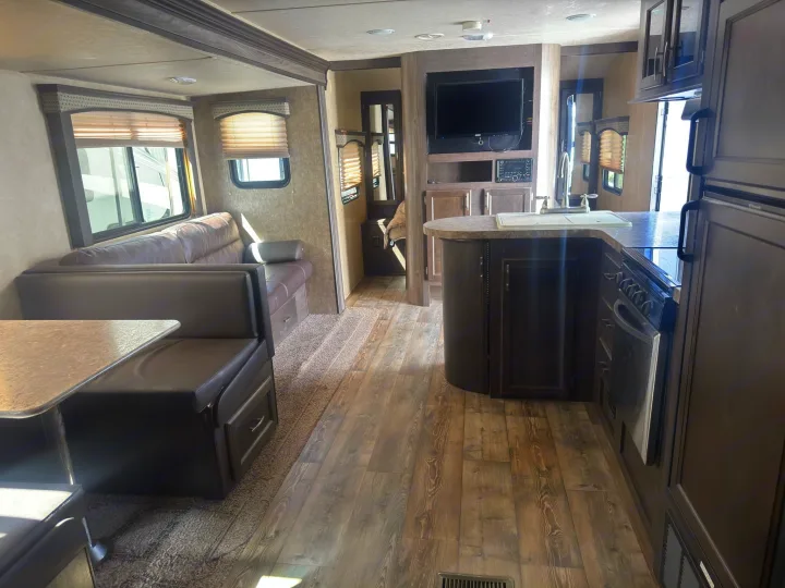 Spacious RV rental interior featuring a living area, dinette, and full kitchen with wood-look floors and dark cabinetry.. Forest River 270BHS 2016