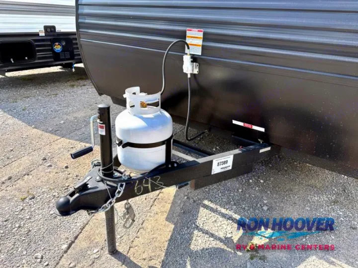 Detail of an RV rental travel trailer's front, showing the hitch, white propane tank, and crank-style jack stand.. Hideout Sport 140RE 2025