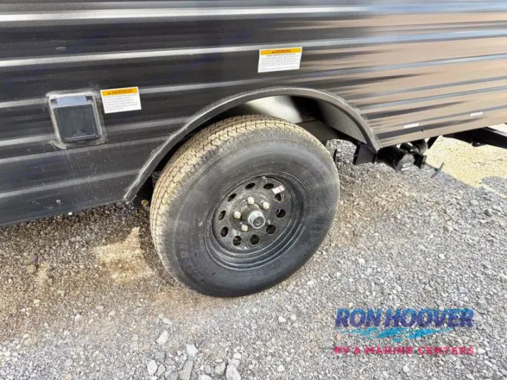 Side of an RV rental travel trailer, featuring its tire, a utility access panel, and plumbing hookups on gravel.. Hideout Sport 140RE 2025