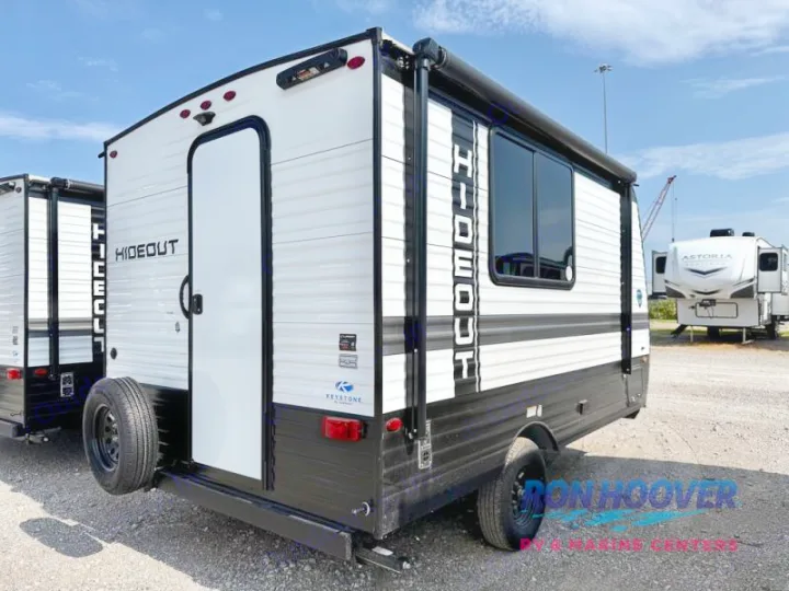 This white and black Hideout travel trailer, perfect for RV rental, features a rear door, side window, and spare tire.. Hideout Sport 140RE 2025