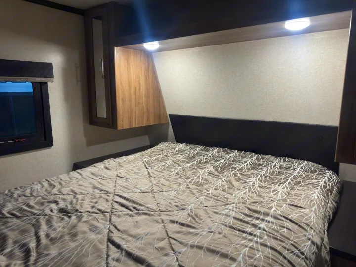 Cozy rv rental bedroom showing a bed with a unique comforter, overhead storage, and bright reading lights.. Jayco Jay Feather 2018