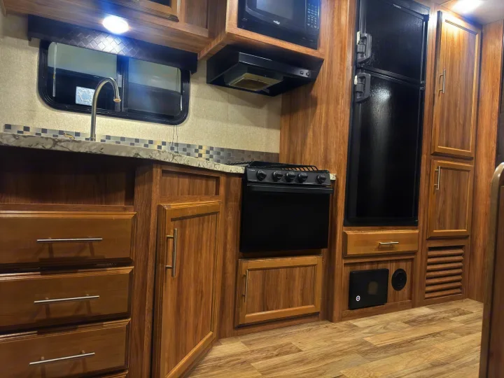 A compact RV rental kitchen showcasing a sink, microwave, stove, fridge, and warm wood cabinets with light countertops.. Jayco Jay Feather 2018