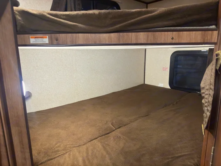 Cozy RV rental bunk beds, a sleeping area inside a camper with a visible warning label and exit sign.. Jayco Jay Feather 2018
