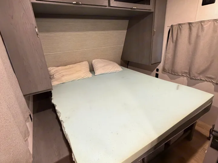 Comfortable RV rental bed with foam topper, pillows, built-in gray cabinetry, and curtains in a cozy camper interior.. Forest River 2690BHK Ozark 2025