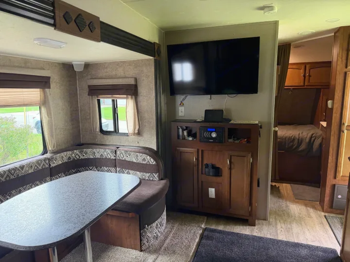 Inside an rv rental, featuring a cozy dining nook, entertainment center with TV, and a peek into the bedroom area.. Coachmen Freedom Express 2017