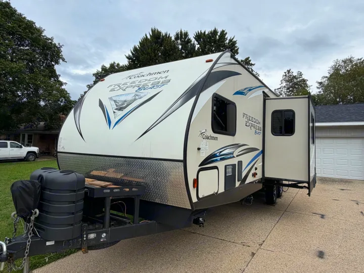A white & blue Coachmen Freedom Express Blast travel trailer with its slide-out open, parked on a driveway, ready for rv rental.. Coachmen Freedom Express 2017