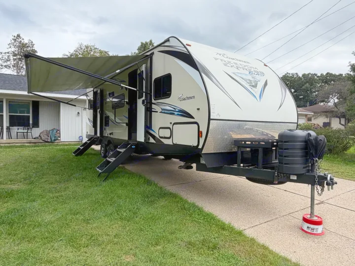 A Coachmen travel trailer rv rental, with its awning out and steps down, parked on a driveway beside a house.. Coachmen Freedom Express 2017