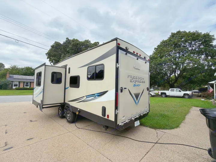 This RV rental, a light-colored "Freedom Express Blast" travel trailer, is parked on a driveway with its slide-out extended.. Coachmen Freedom Express 2017