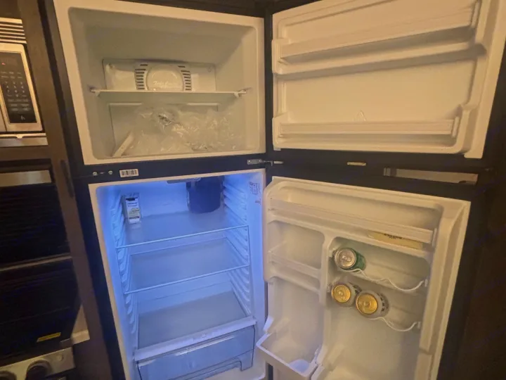 Open two-door refrigerator in an RV rental. The top freezer has a plastic bag, while the fridge door holds a few cans.. Forest River Salem 2022
