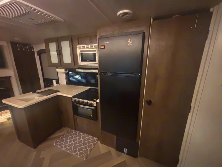 Modern rv rental kitchen featuring a black refrigerator, microwave, stove with oven, and sink in a compact layout.. Forest River Salem 2022