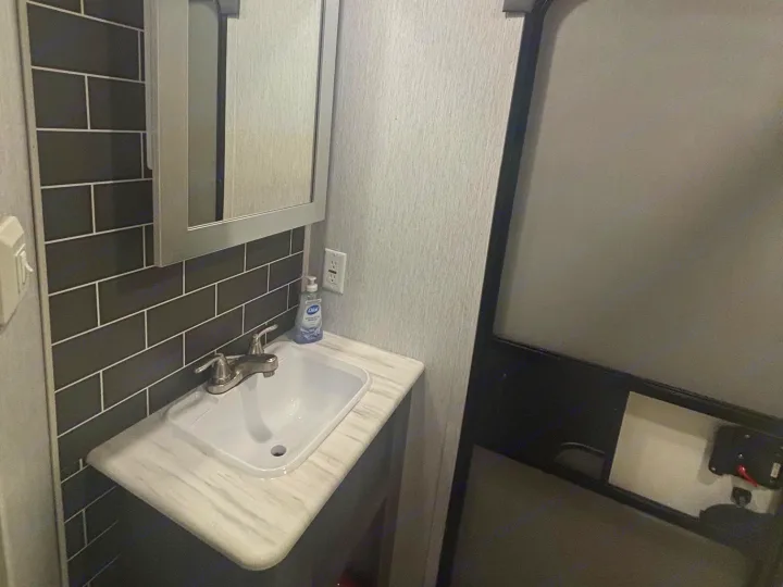 Compact RV rental bathroom features a vanity with dark subway tile backsplash, white sink, and mirror. Hand soap and outlet visible.. Forest River Salem 2022