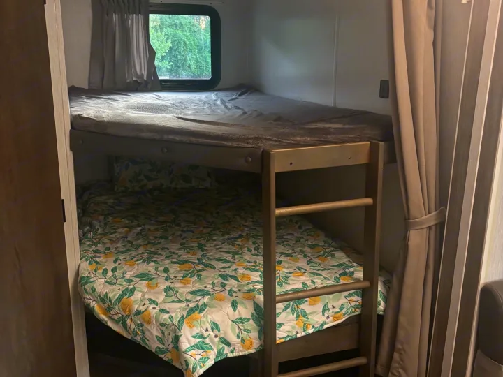 Relax in your rv rental: a cozy bunk bed setup with a grey blanket on top and a lemon-print quilt below, by a window.. Forest River Salem 2022
