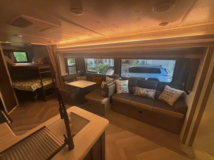 Interior of an RV rental: living area with sofa, dining table, kitchen sink, and bunk beds. Enjoy comfortable travel.. Forest River Salem 2022