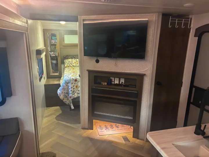 Cozy rv rental interior: living area with TV and fireplace, looking into a bedroom, and a peek of the kitchen counter.. Forest River Salem 2022