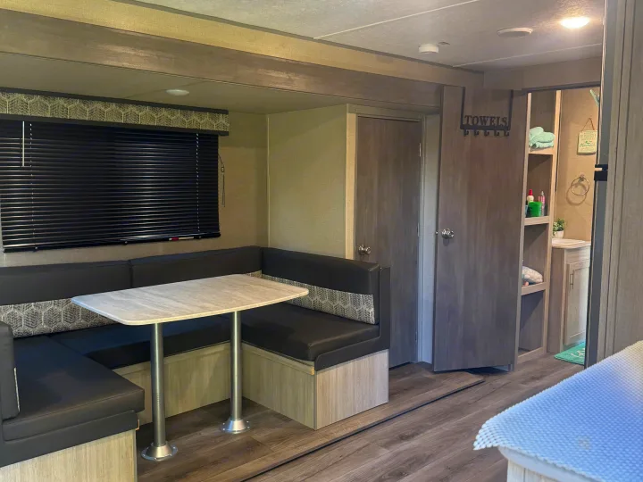 Cozy RV rental dinette with U-shaped seating, table, and a glimpse into the organized bathroom area.. Coachmen Catalina summit series 8 2023