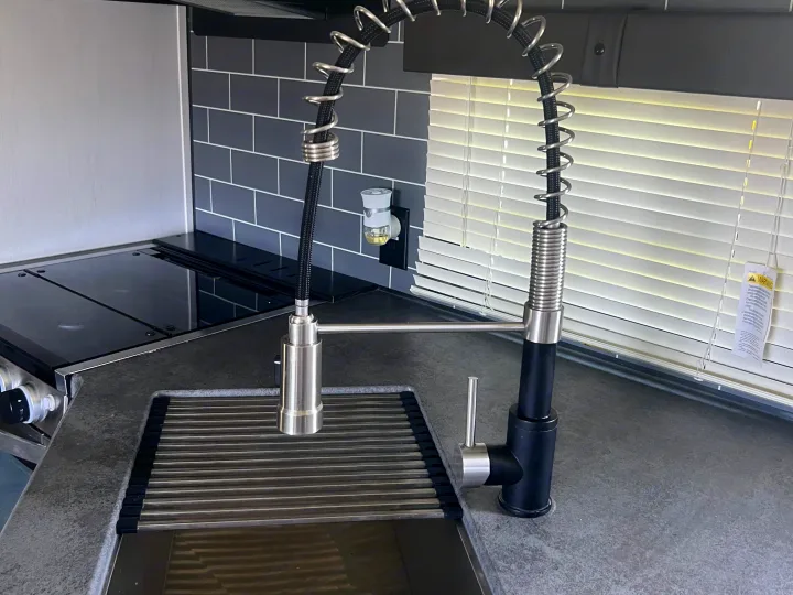 Modern RV rental kitchen with a black/silver faucet, grey speckled countertop, dark subway tile backsplash, and drying rack.. Forest River Palomino Puma 2021