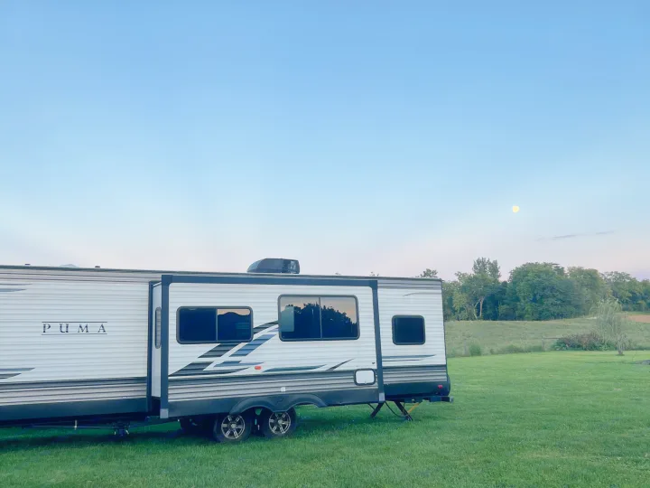 Enjoy an RV rental: a Puma travel trailer parked on a green field under a clear, moonlit evening sky, surrounded by nature.. Forest River Palomino Puma 2021