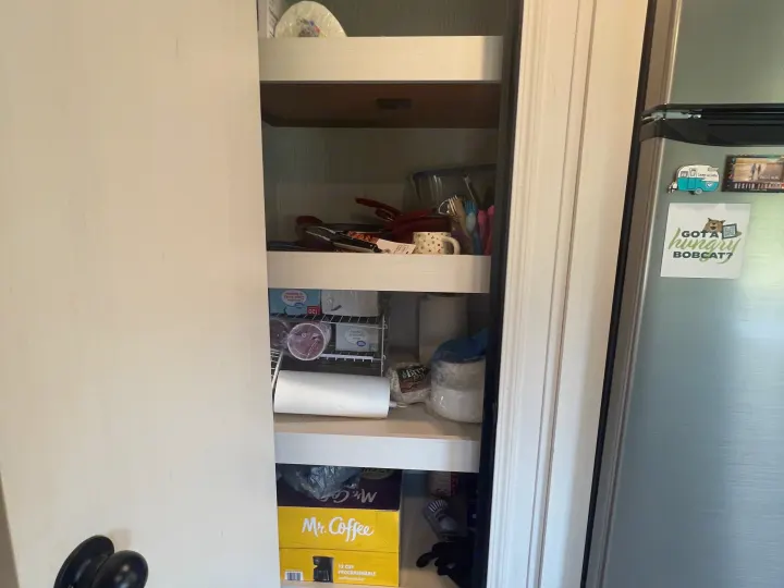 Organized RV rental pantry with shelves of kitchen supplies, paper towels, and a Mr. Coffee box, beside a fridge with magnets.. Forest River Palomino Puma 2021