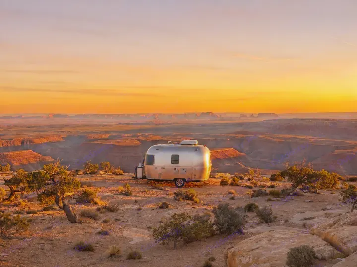 A silver Airstream RV rental is parked at sunset, overlooking a vast, orange-hued canyon landscape.. Airstream Bambi 2022