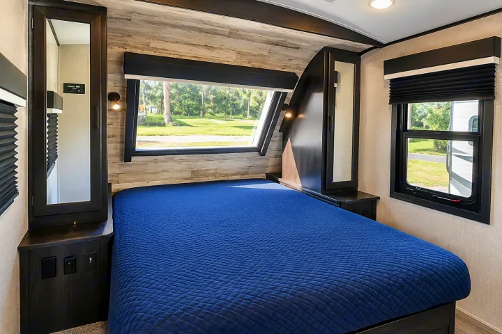 Spacious rv rental bedroom featuring a blue bed, large windows with scenic views, and integrated storage with outlets.. Jayco White Hawk 2022